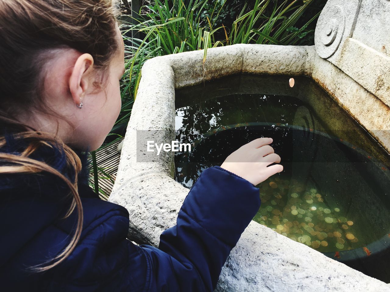 High angle view of girl throwing coin in wishing well