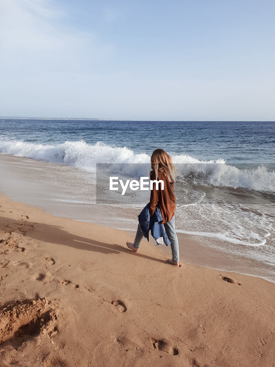 Rear view of woman walking on the beach against clear sky