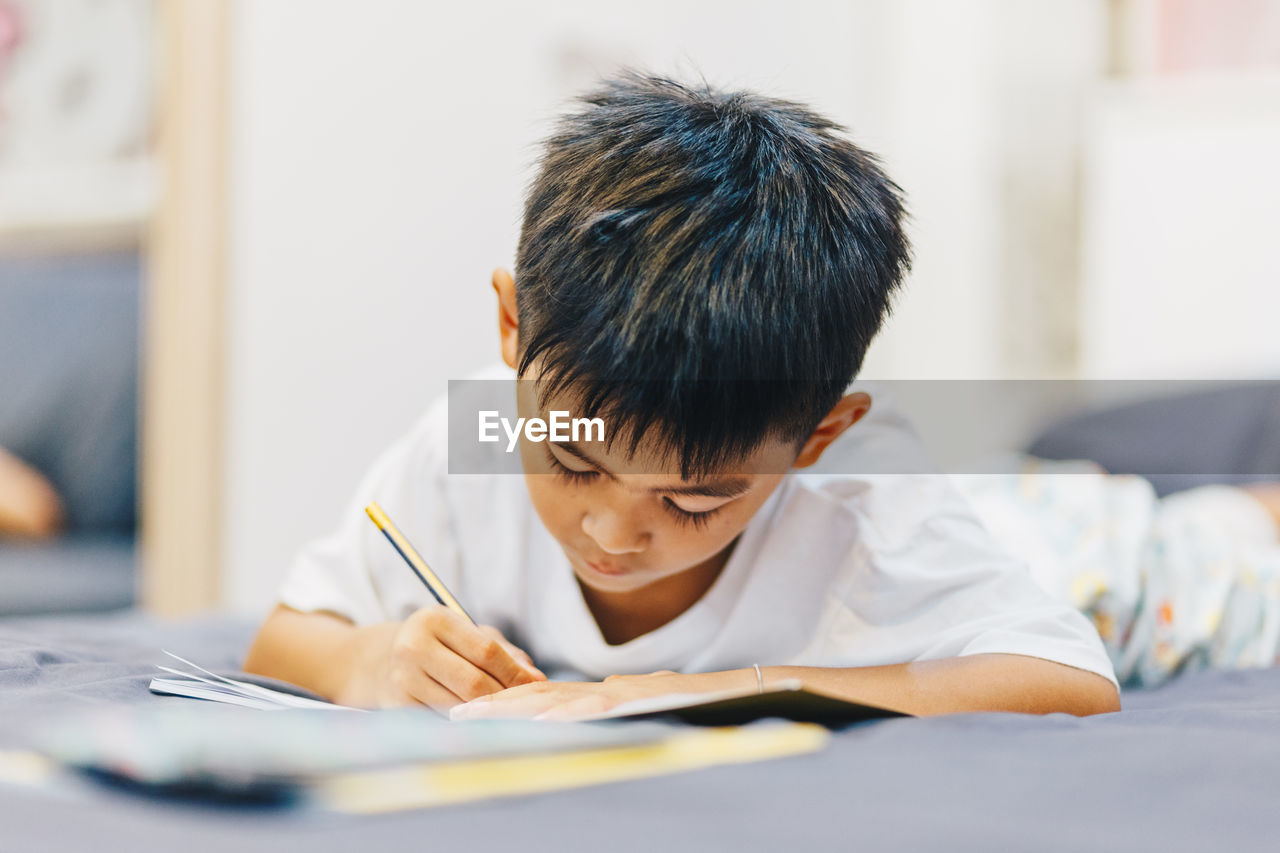 Cute boy writing in book at home