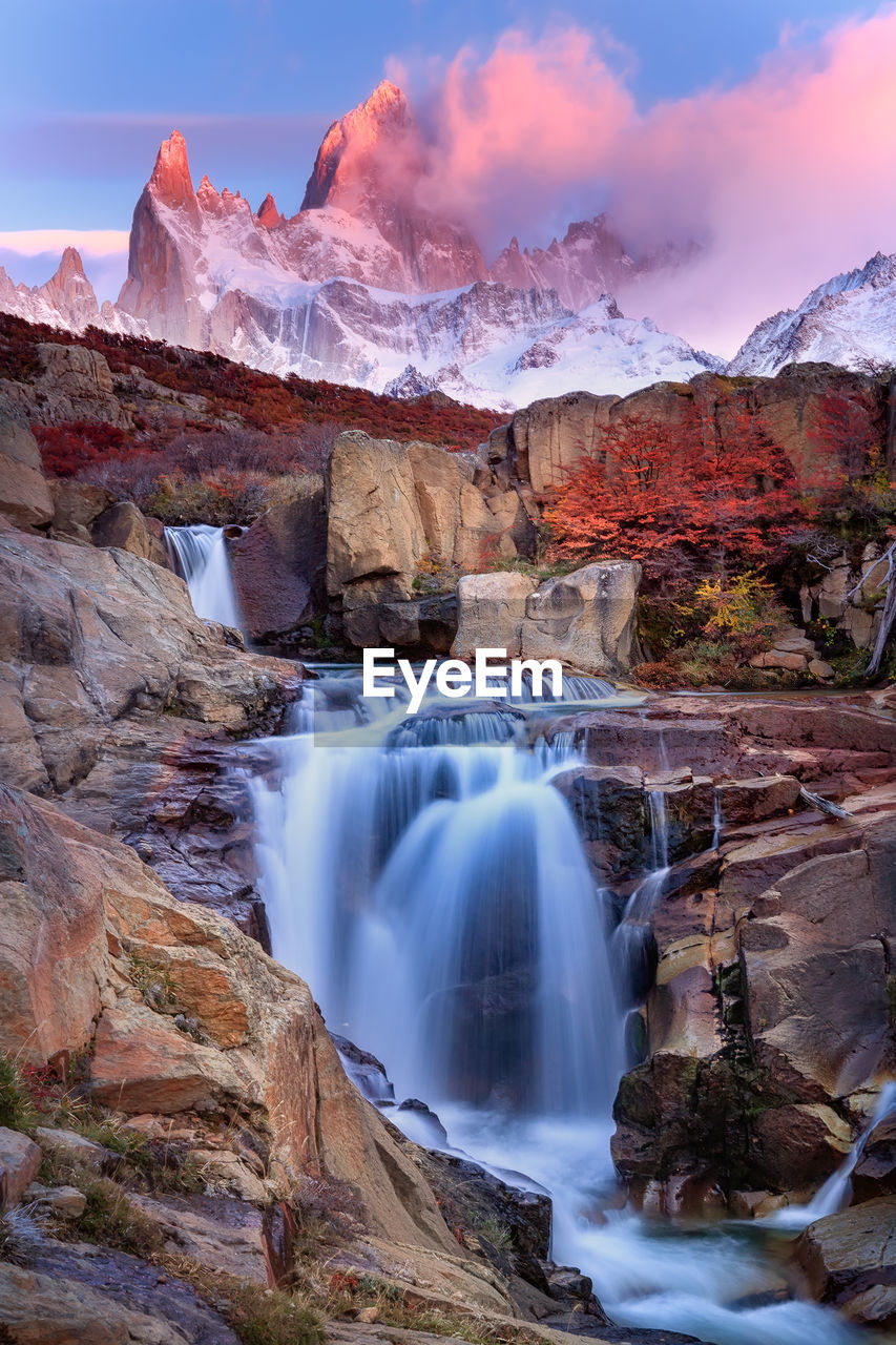 SCENIC VIEW OF WATERFALL AGAINST MOUNTAINS