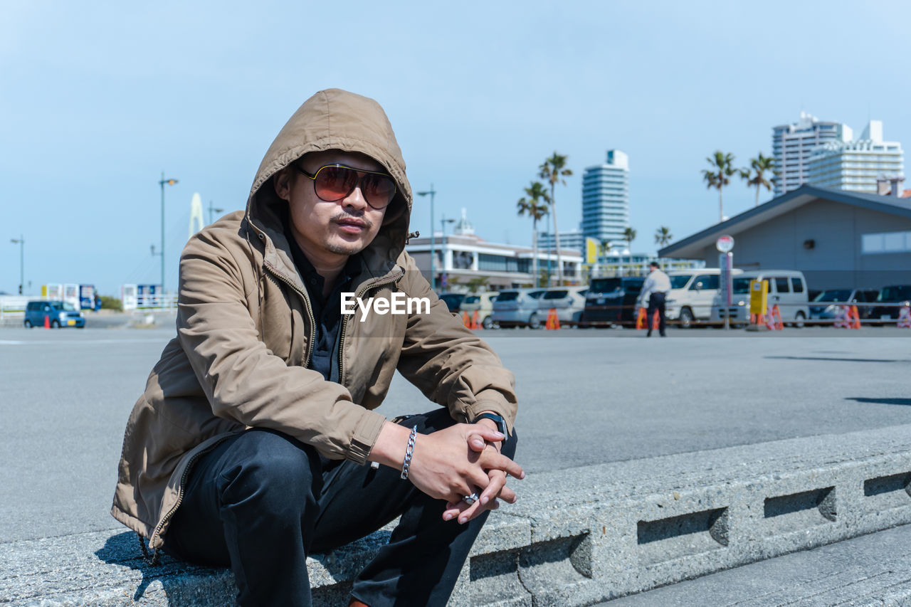 Portrait of man sitting in city against sky