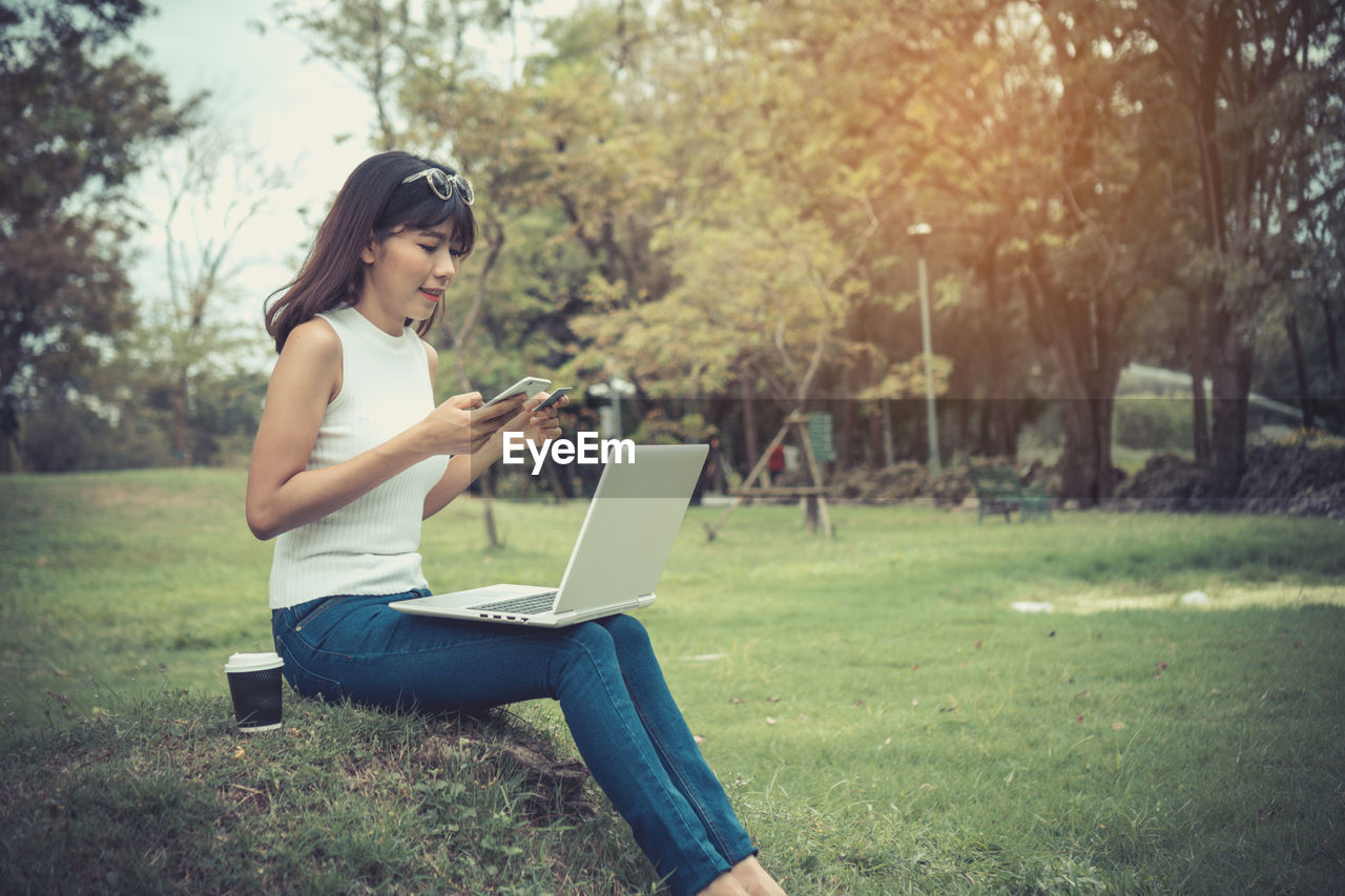 Young woman doing online shopping while sitting on grassy field