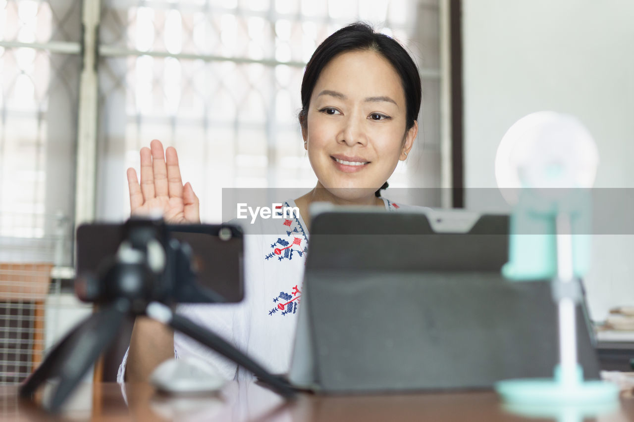 Woman waving hand greeting viewer using smartphone online broadcasting live.