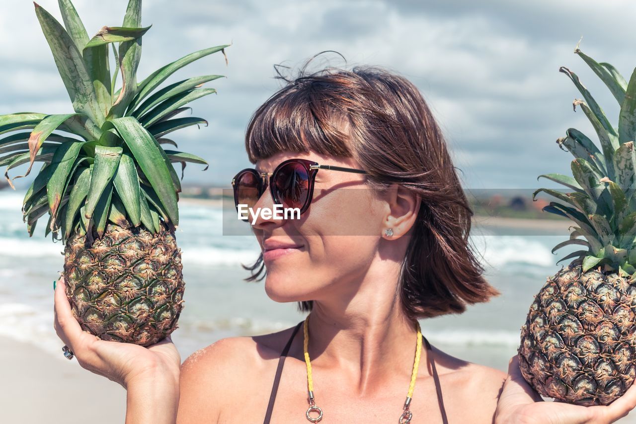 Smiling young woman holding pineapples at beach