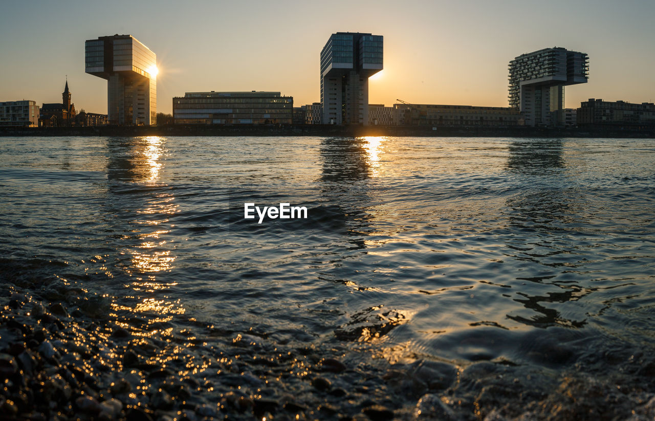 SEA BY BUILDINGS AGAINST SKY DURING SUNSET