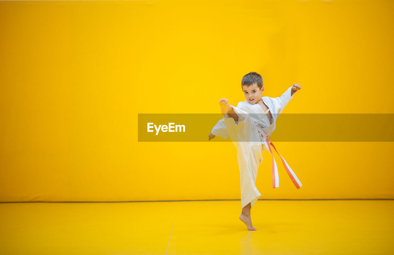 Portrait of cute boy practicing martial arts against yellow wall