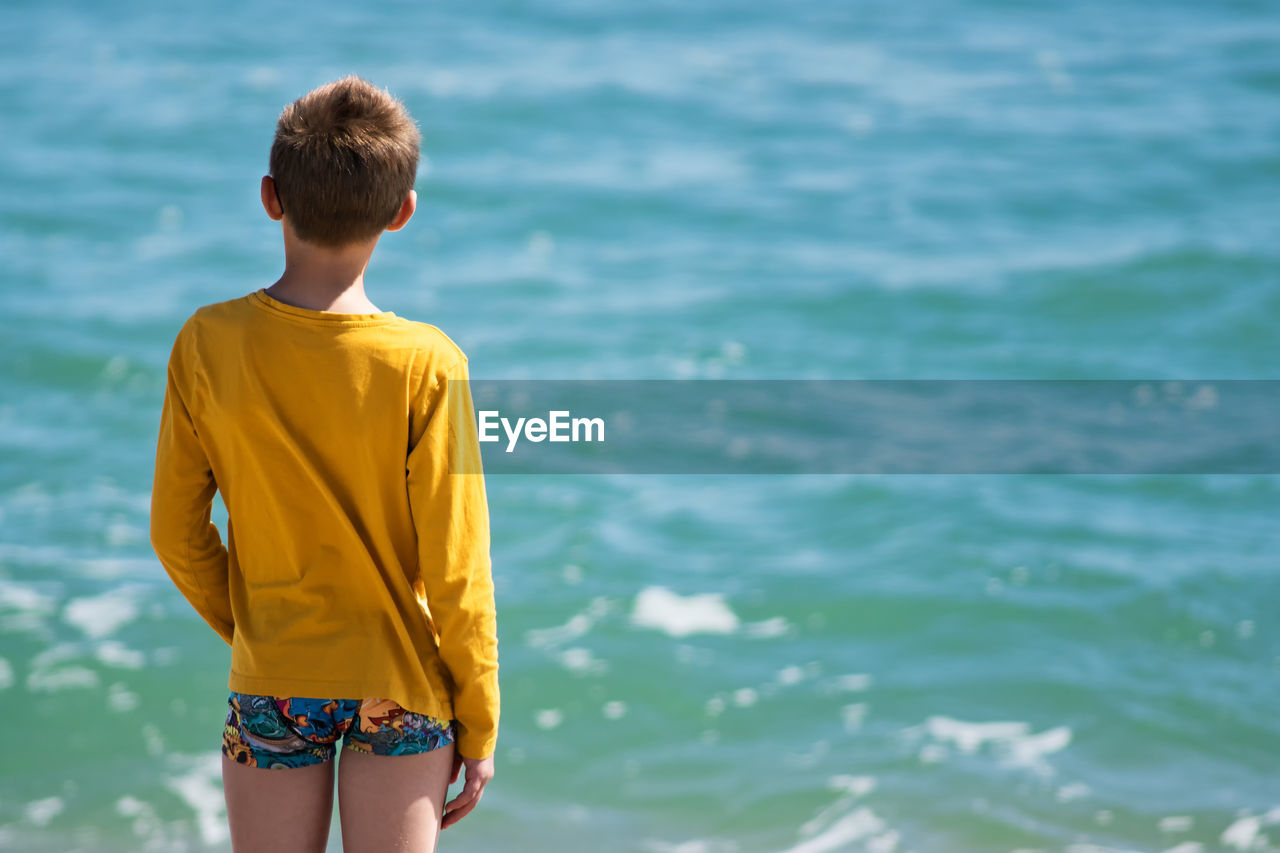 Rear view of boy standing against sea