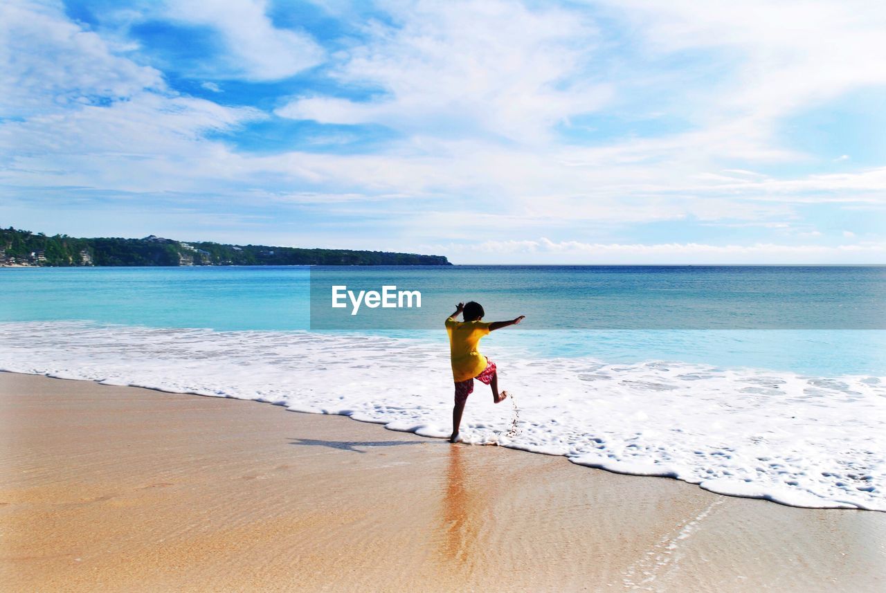 Rear view of boy kicking surfing reaching on shore