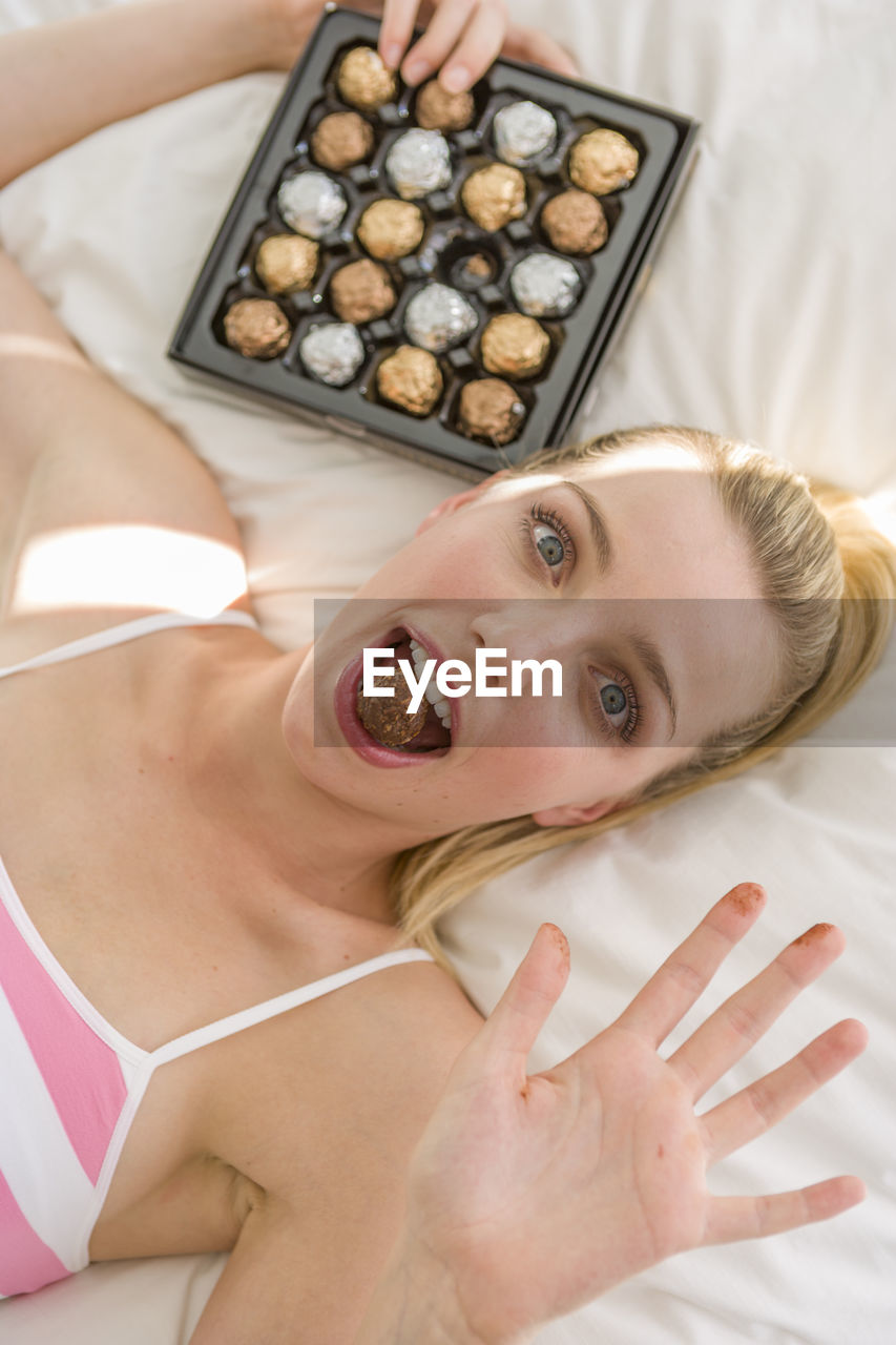 Portrait of woman eating chocolate while gesturing stop sign at home