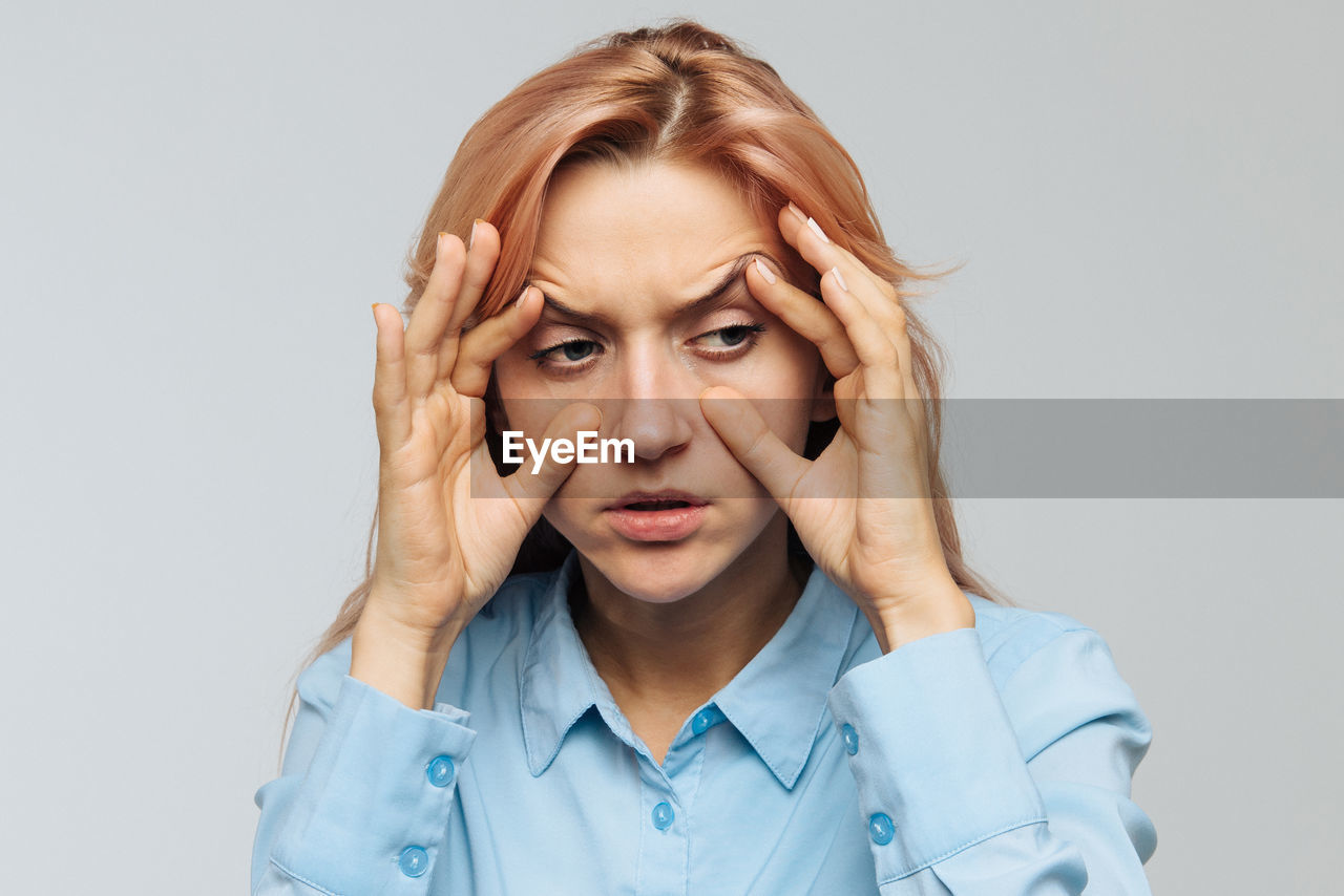 Woman stretching eyes against gray background