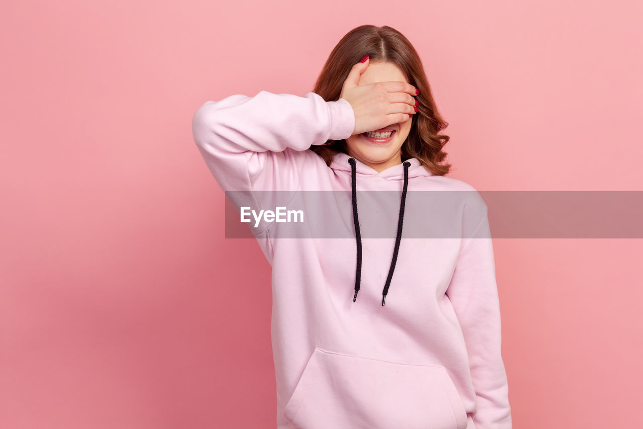 FULL LENGTH OF WOMAN STANDING AGAINST PINK WALL