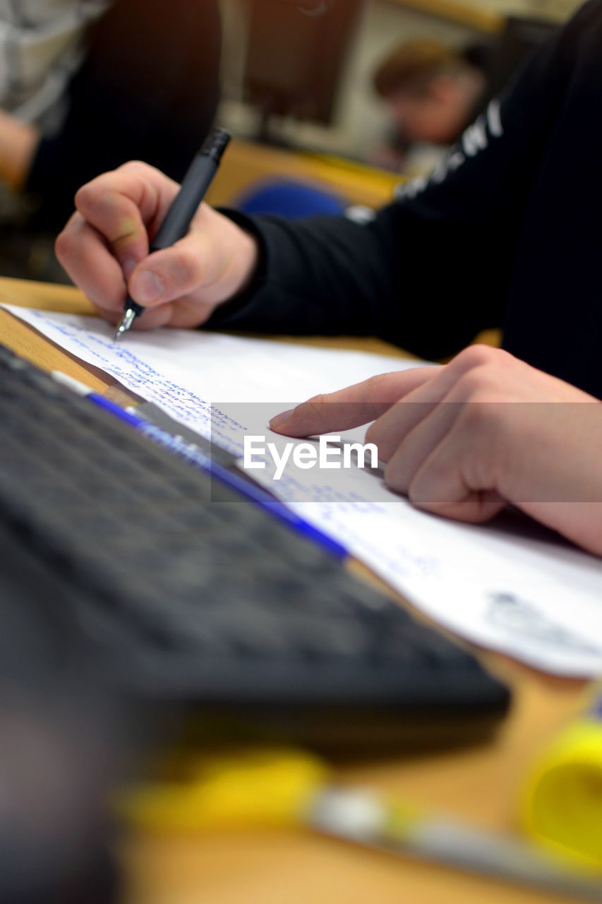 Cropped image of person writing in notebook by computer keyboard at school