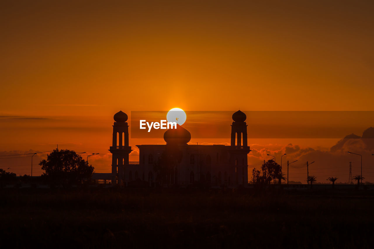 SILHOUETTE BUILDING ON FIELD AGAINST ORANGE SKY