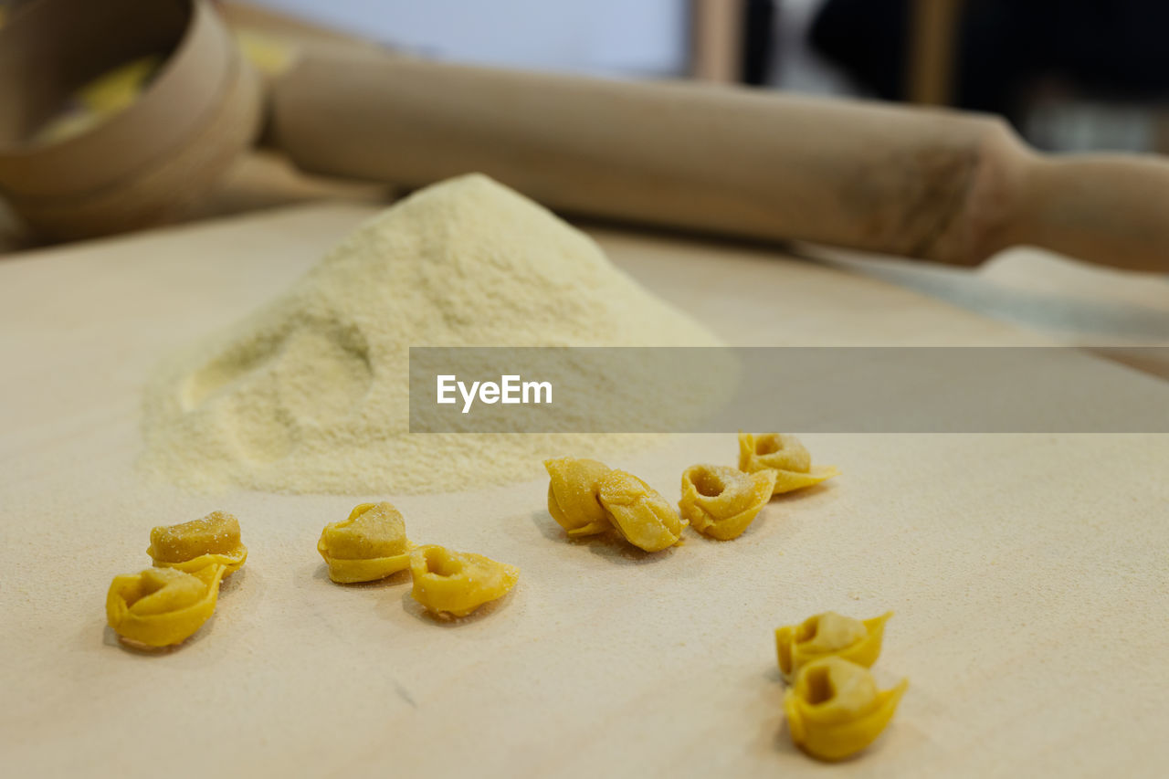 Freshly made raw tortellini over wooden table and a rolling pin and flour in the background.