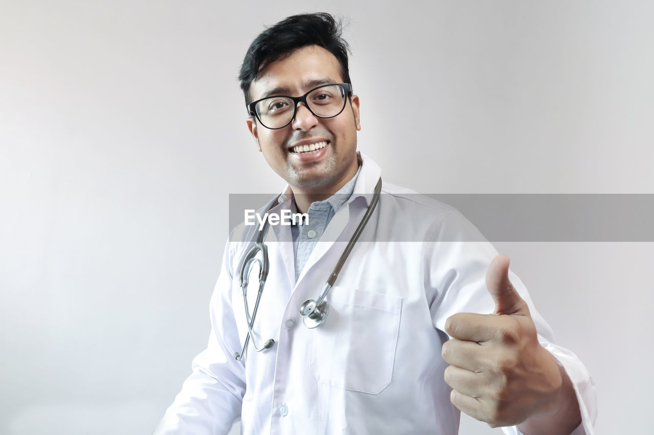 Portrait of smiling doctor showing thumbs up against white background