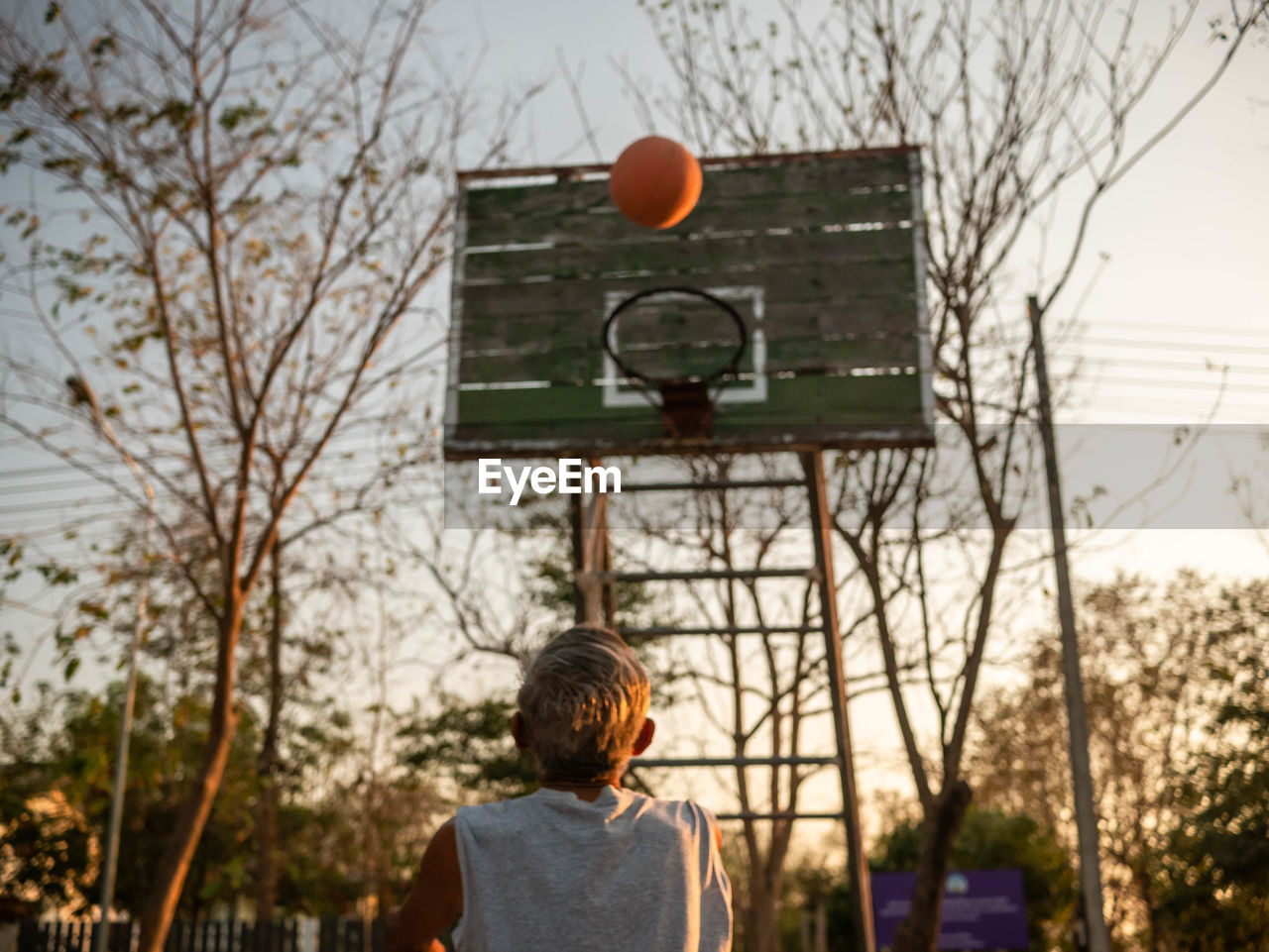 Rear view of senior man playing basketball at sunset