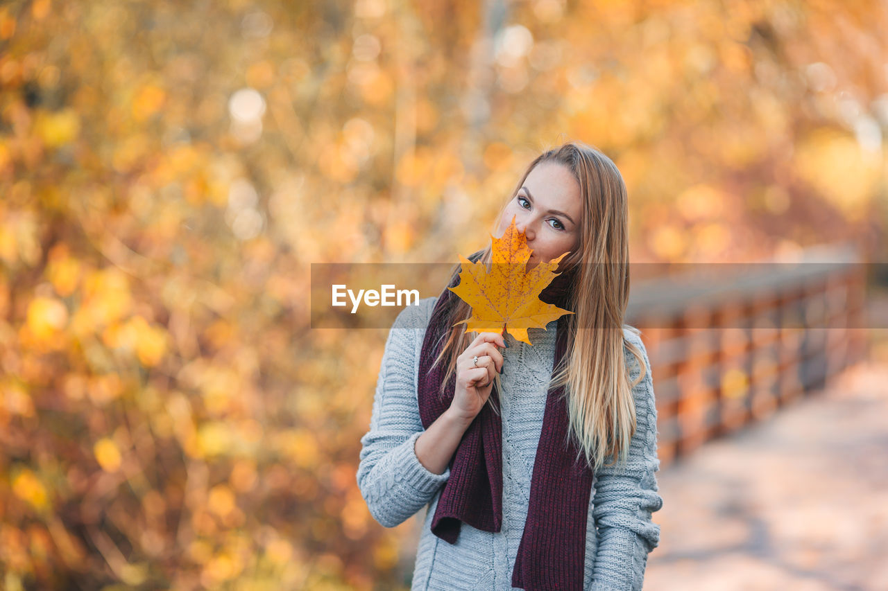 Close-up of woman holding autumn leaf against tree