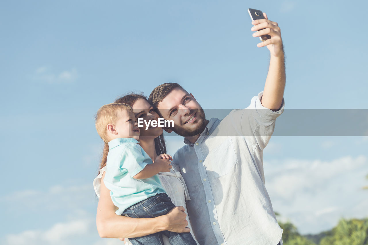 Family taking selfie through mobile phone while standing against sky