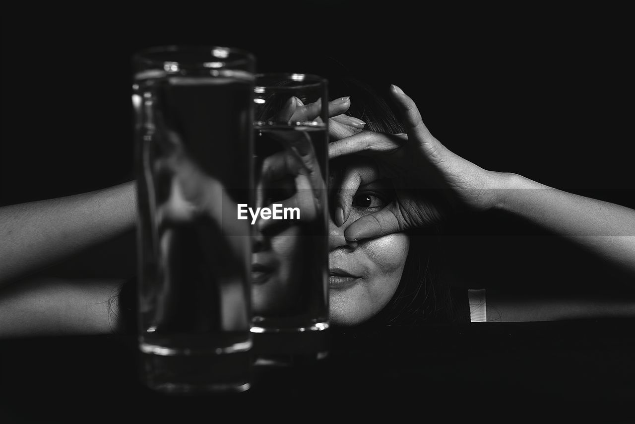 Close-up of woman gesturing over eyes seen through glasses of water 