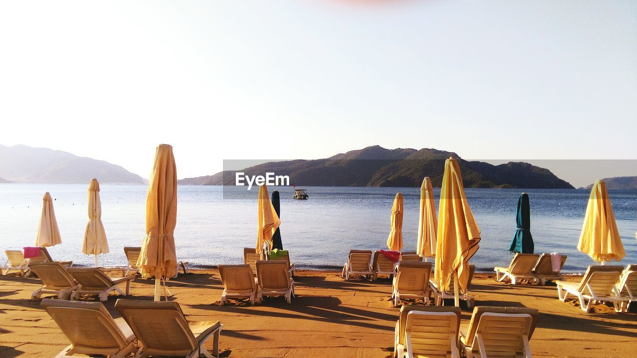 Deck chairs with parasols at beach against clear sky