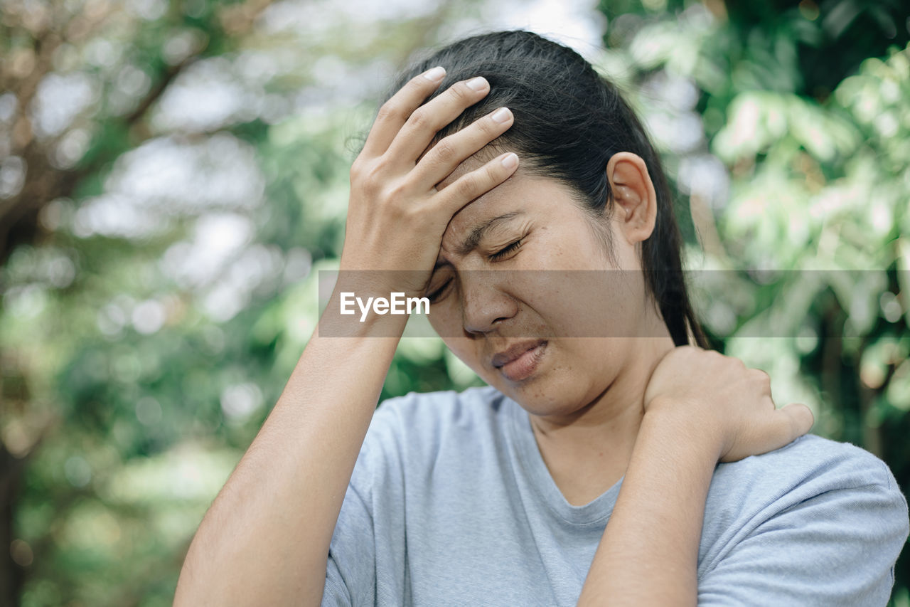 Woman touching head in pain against trees