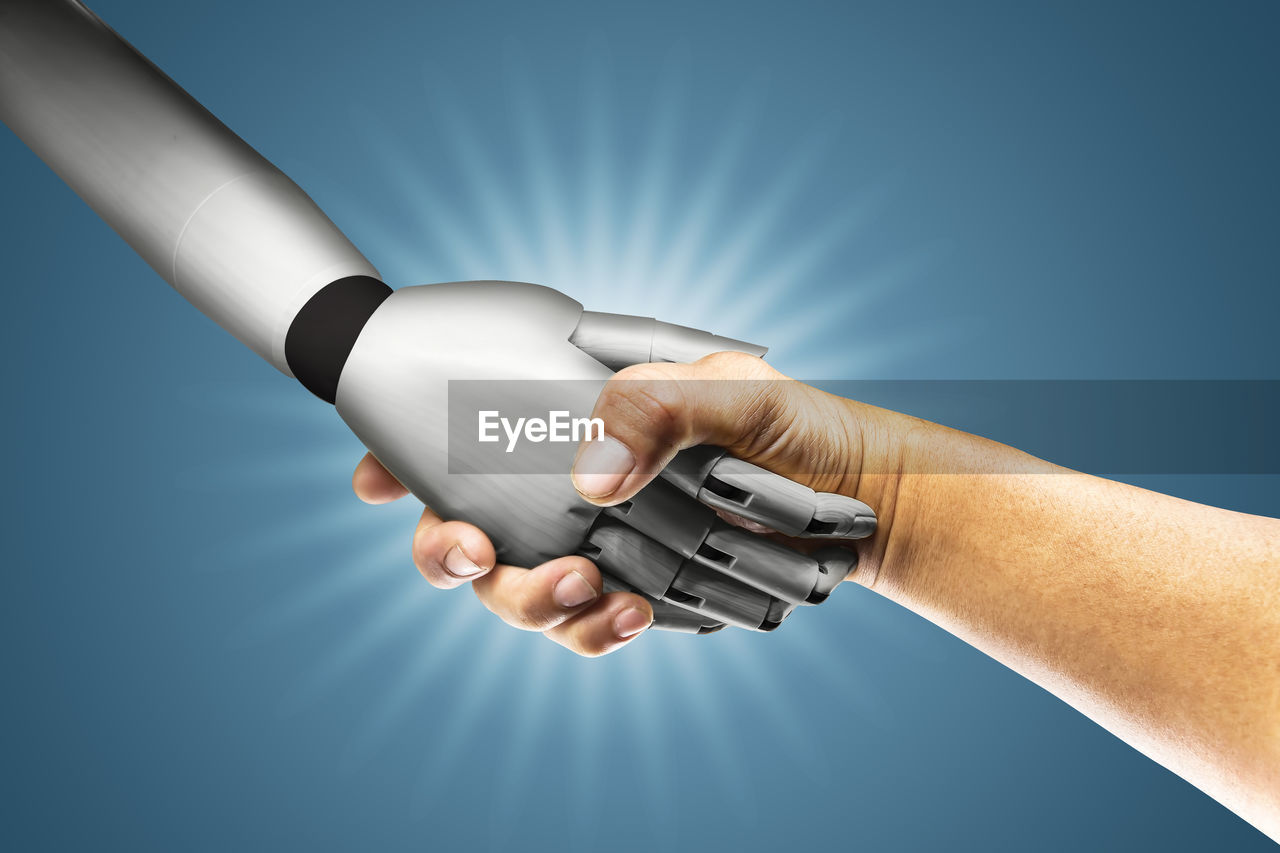 Cropped image of person handshaking with robot hand over blue background