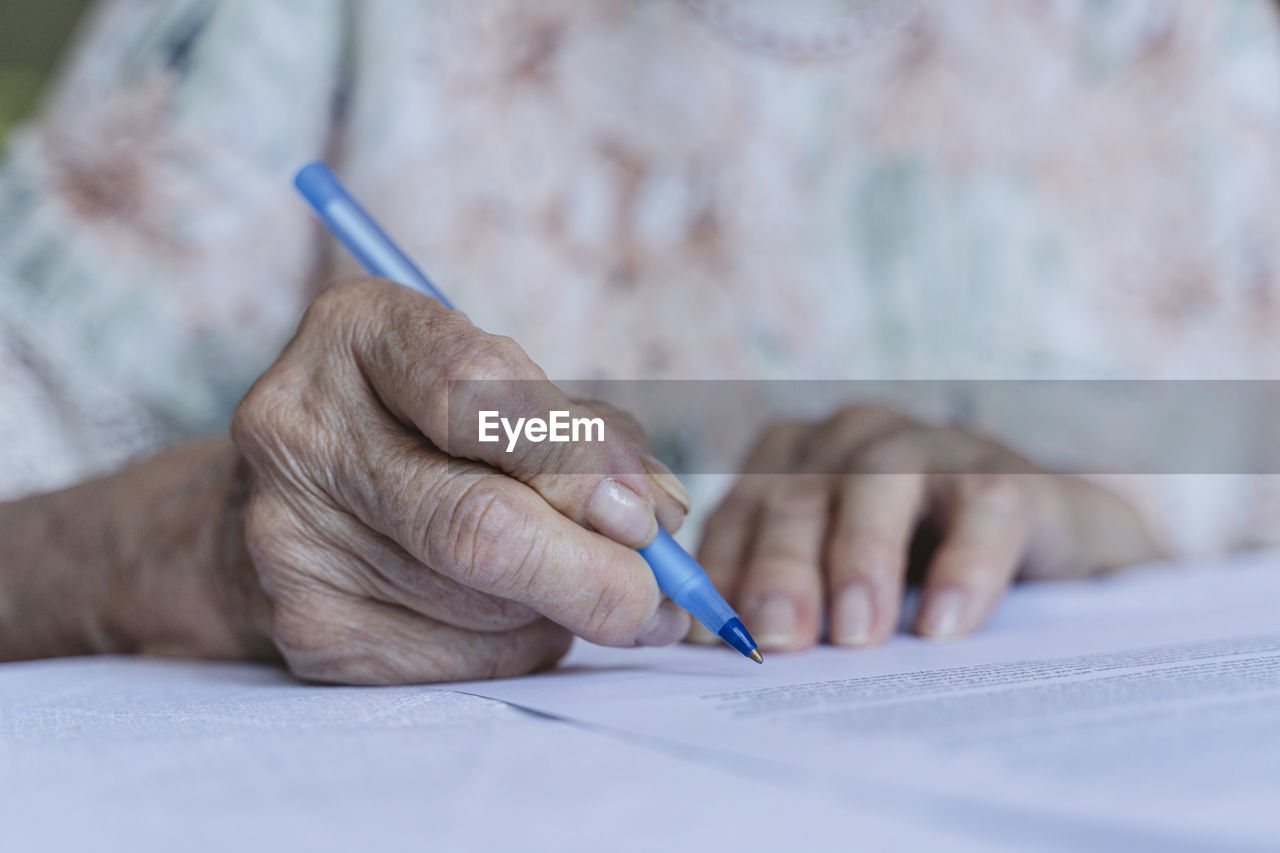 Wrinkled hand of senior woman signing agreement papers at home