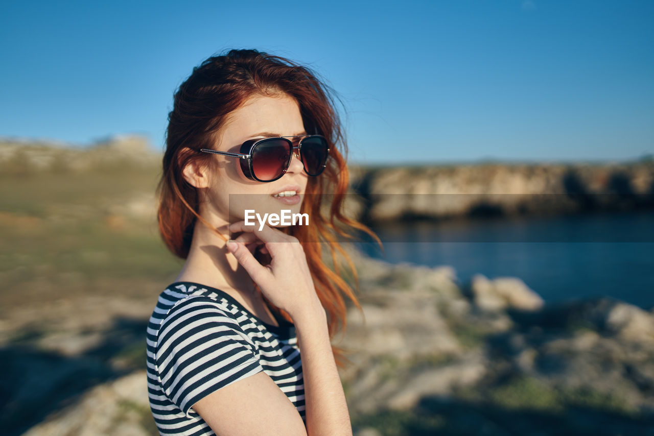 PORTRAIT OF YOUNG WOMAN WEARING SUNGLASSES STANDING ON LAND