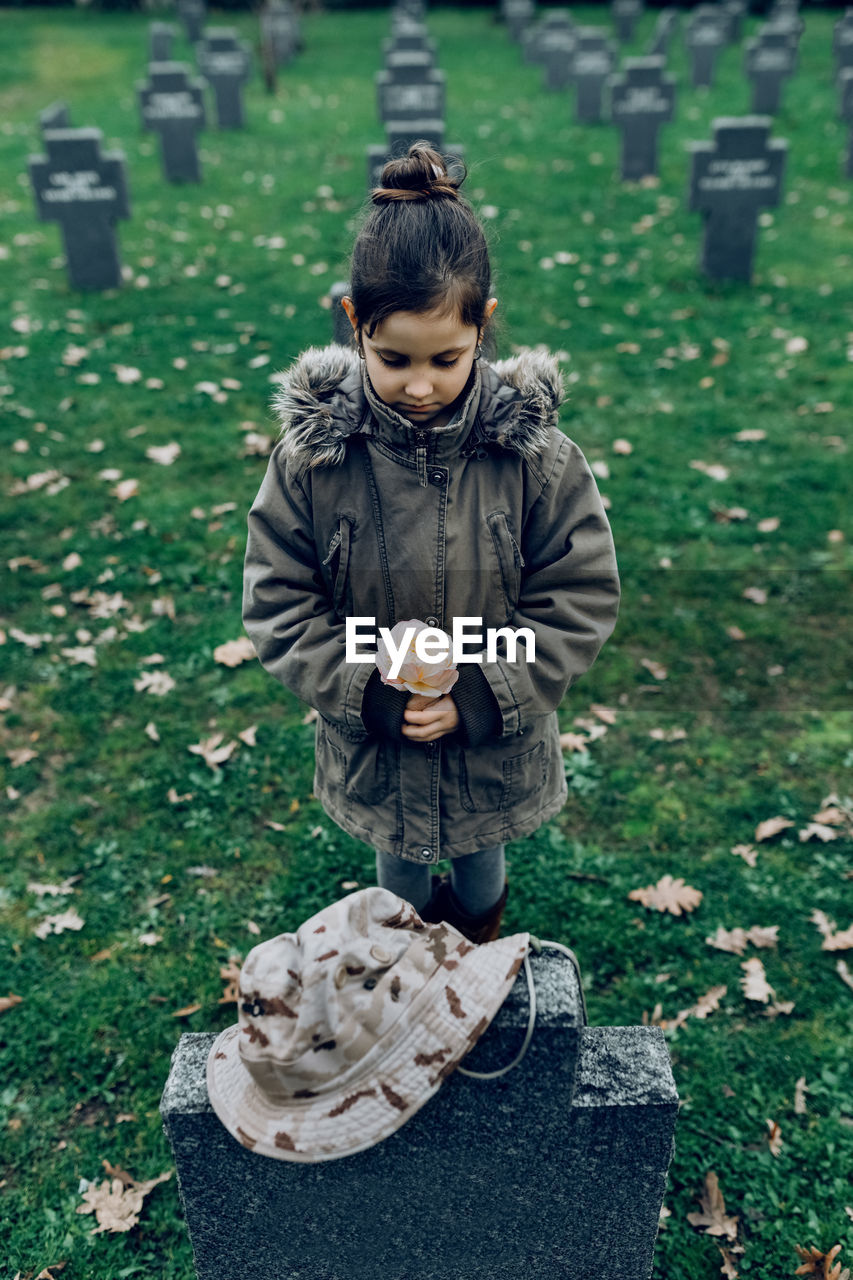 High angle of small kid mourning death of soldier fighting in war at graveyard