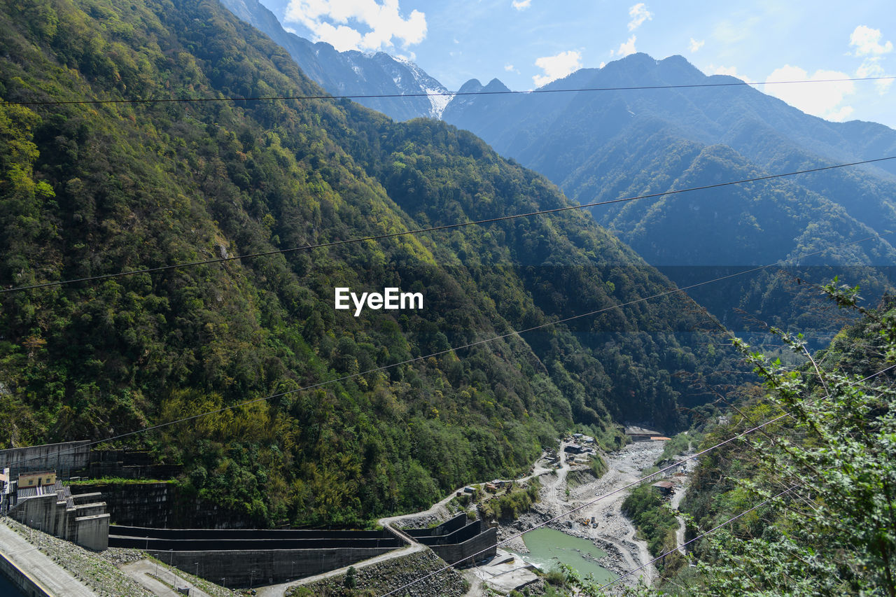 mountain, scenics - nature, environment, beauty in nature, mountain range, plant, landscape, nature, tree, mountain pass, land, sky, architecture, travel, travel destinations, forest, tranquility, tranquil scene, no people, built structure, cloud, valley, non-urban scene, outdoors, day, tourism, green, environmental conservation, high angle view, idyllic, transportation, pine tree, pinaceae, road, social issues, mountain peak, coniferous tree, adventure, pine woodland, walking, sunlight