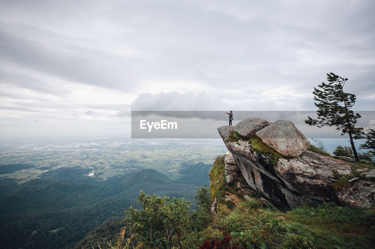Hiker standing on cliff against cloudy sky during foggy weather