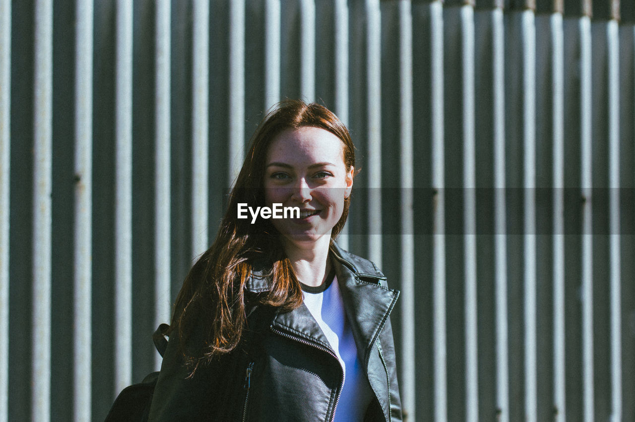 Portrait of smiling young woman standing against metal wall