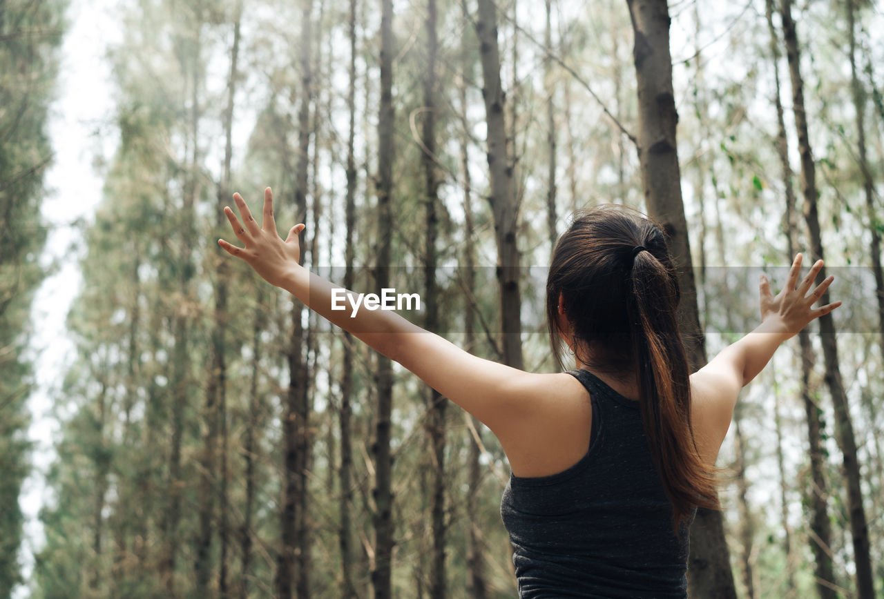 Rear view of successful female athlete standing with arms outstretched in forest