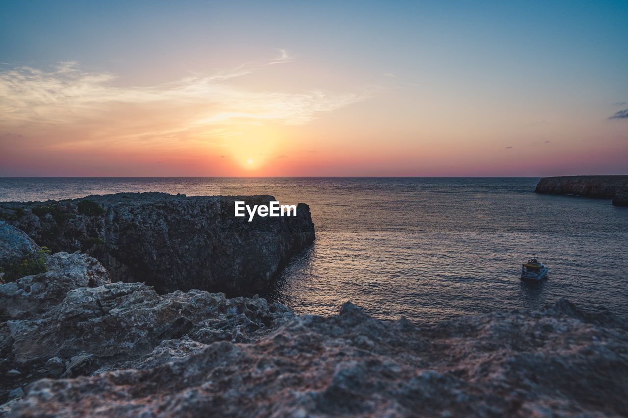SCENIC VIEW OF ROCKS IN SEA AGAINST SKY DURING SUNSET