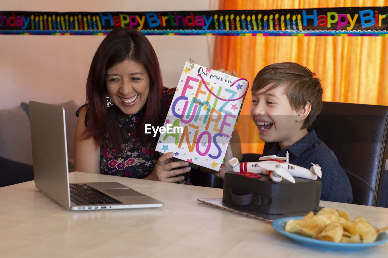 SMILING YOUNG WOMAN USING SMART PHONE AT TABLE