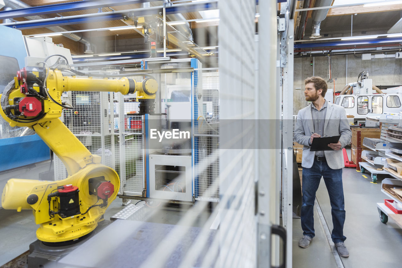 Businessman looking at industrial robot in modern factory
