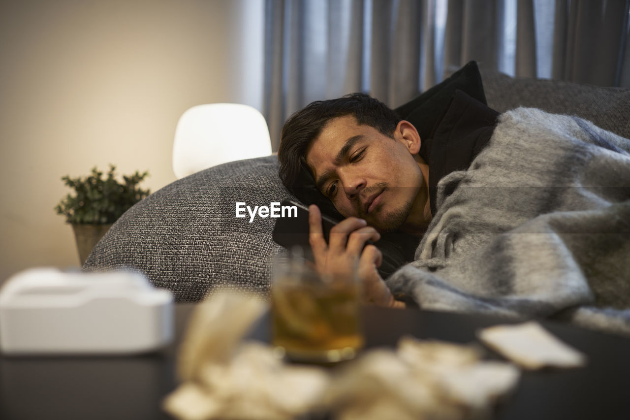 Young man lying on sofa and using smart phone