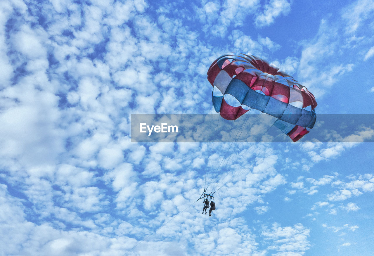 Low angle view of people paragliding against sky