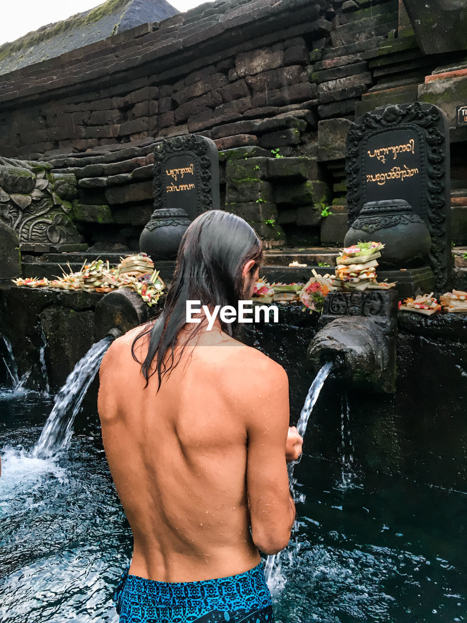 Shirtless man standing in water at temple