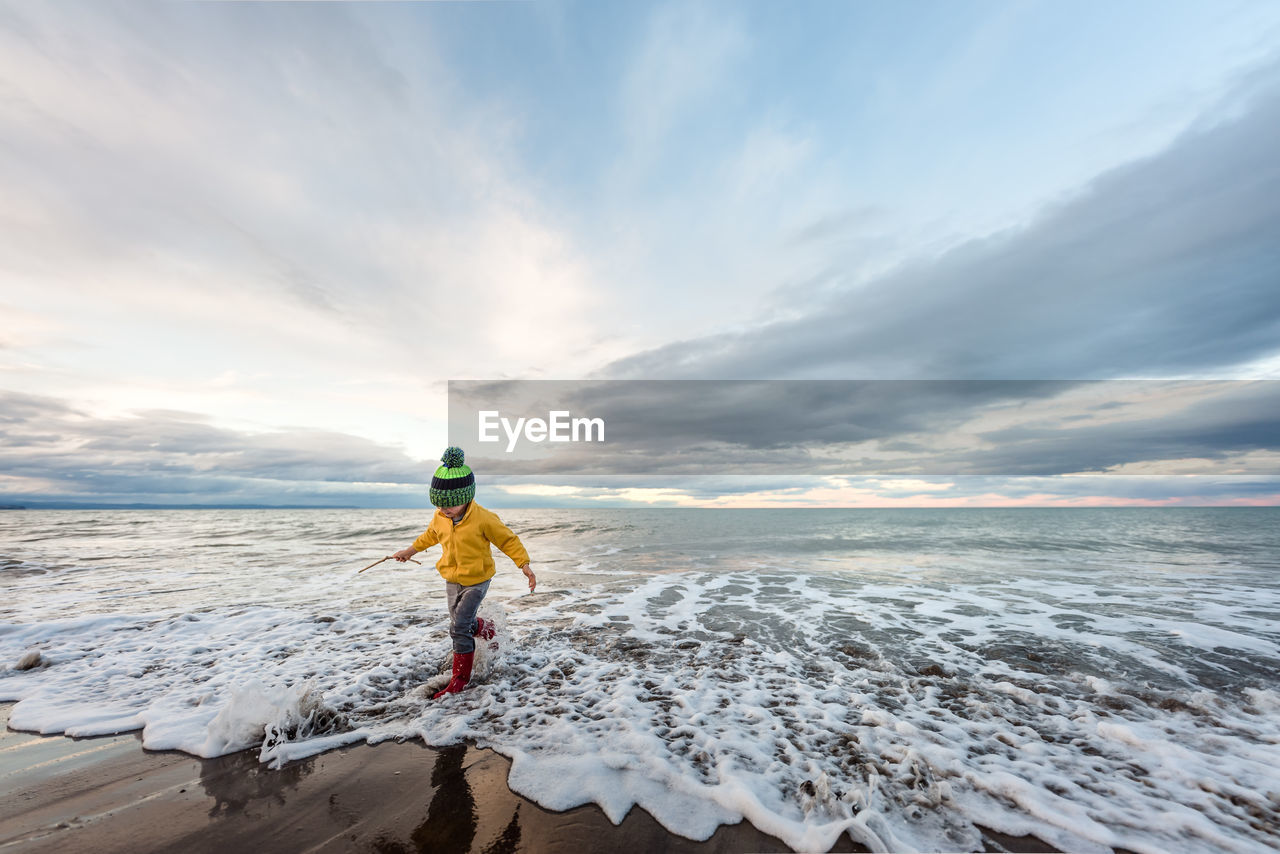 Preschooler running in water with boots and hat in new zealand