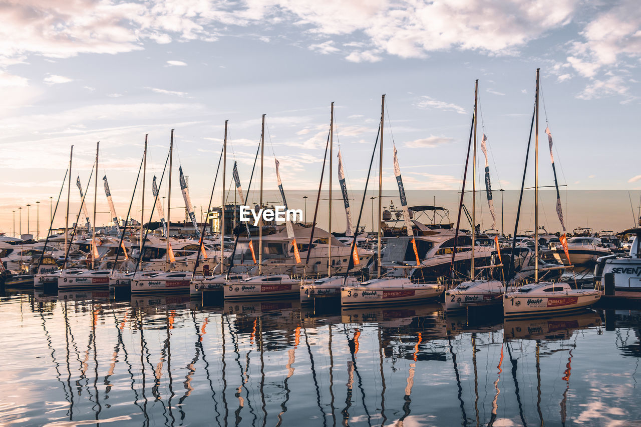 Sailboats moored at harbor against sky during sunset