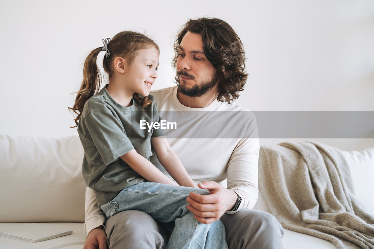 Young happy family with father and daughter on sofa in cozy home, father day
