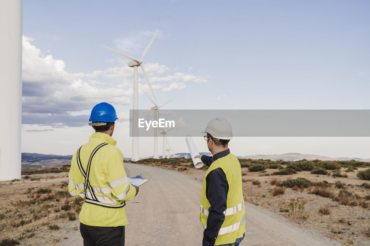 Technicians discussing on road looking at wind turbines at wind farm