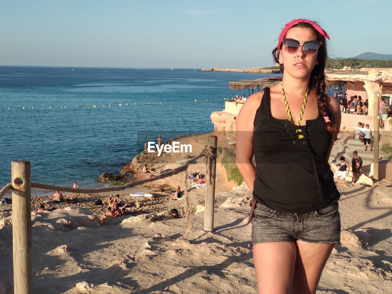 YOUNG WOMAN WEARING SUNGLASSES STANDING AT BEACH