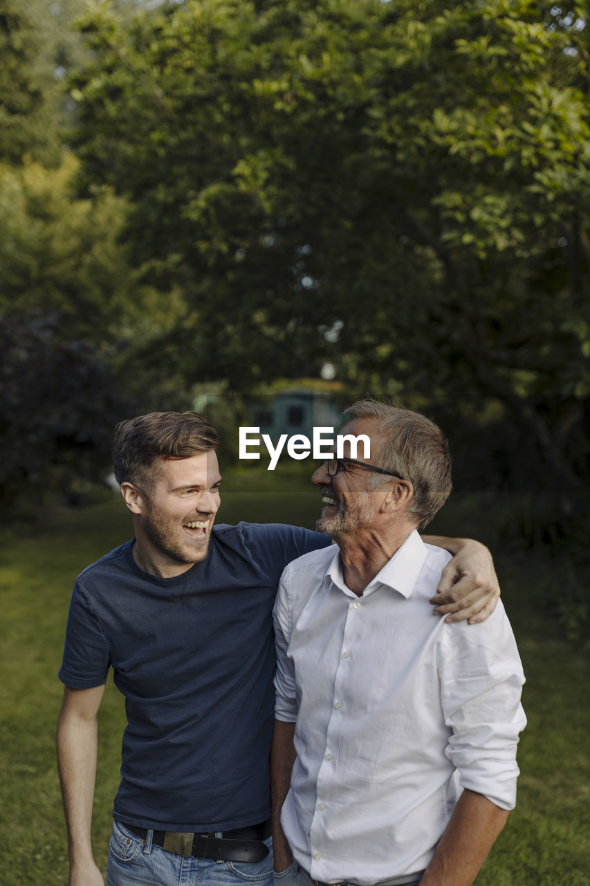 Laughing son embracing father while standing at backyard