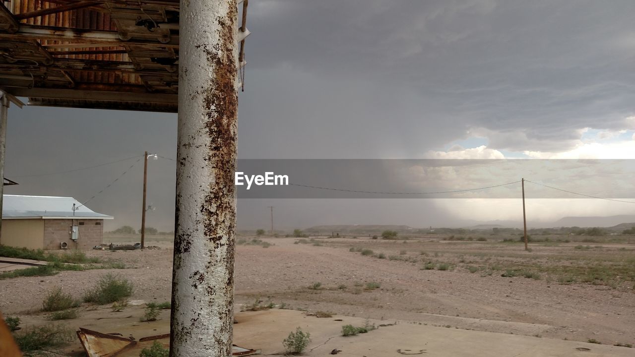 Metal column of abandoned stilt house on field against storm clouds