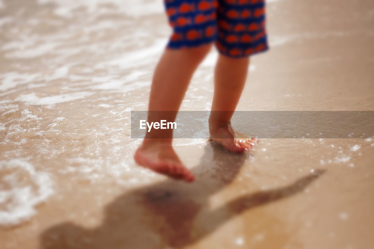 LOW SECTION OF BOY STANDING IN WET WATER