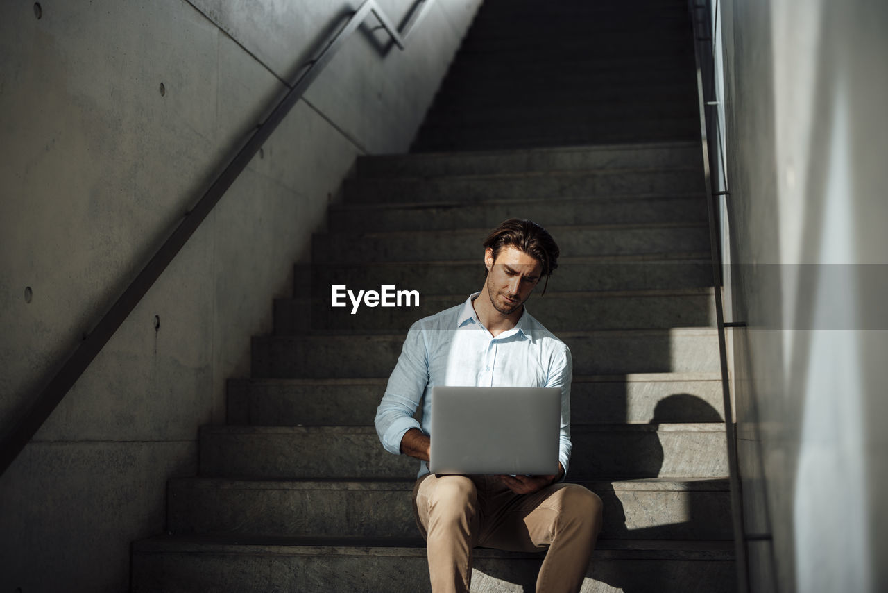 Businessman using laptop sitting on steps