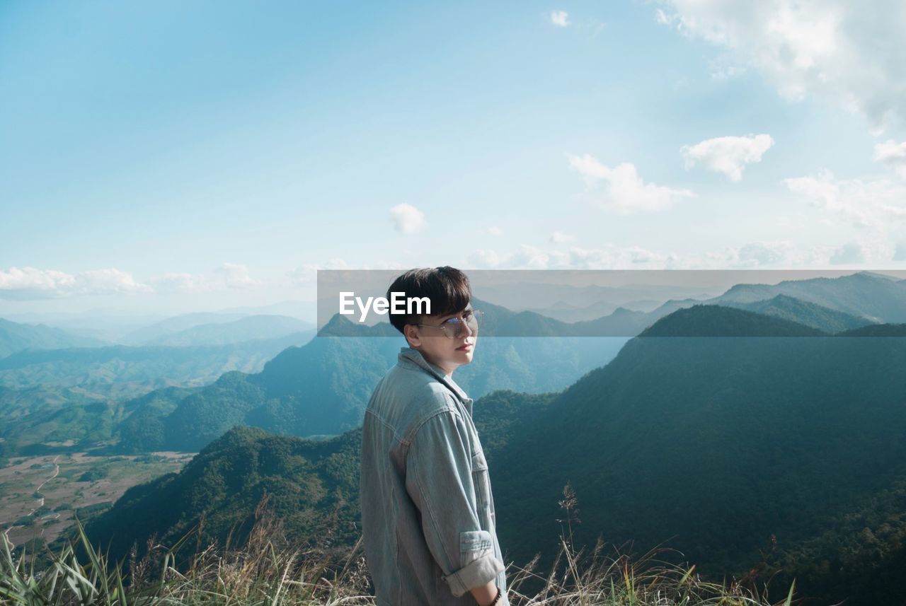 Portrait of young man standing on mountain against sky