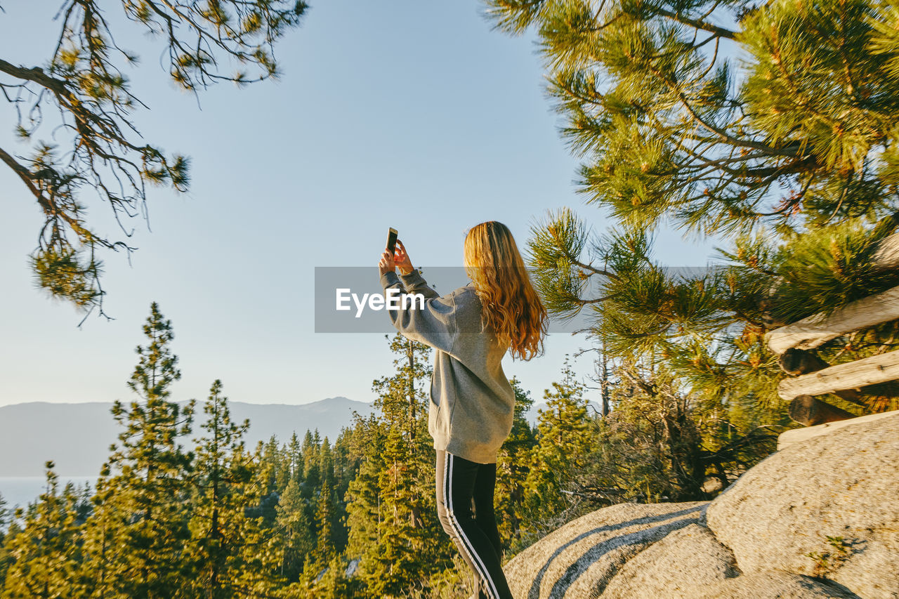 Young woman taking a picture of sunset over lake tahoe.
